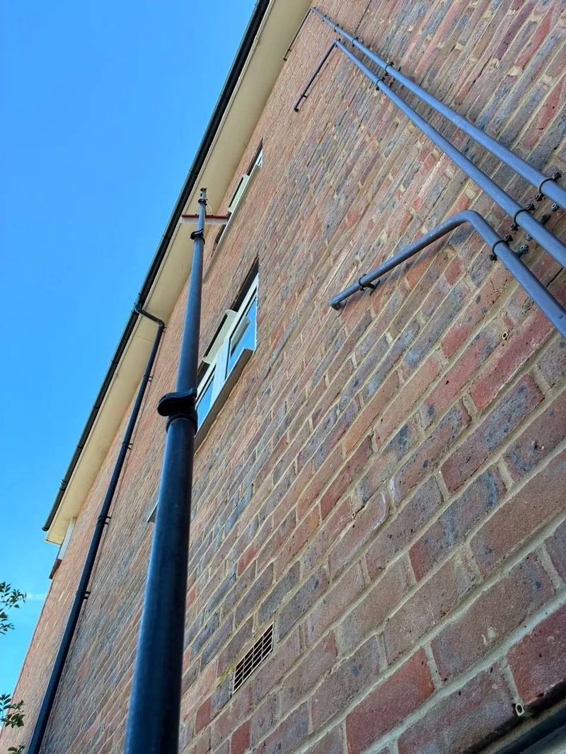 Looking up a brick wall at a water fed pole reaching the white fascia and soffit under a blue sky