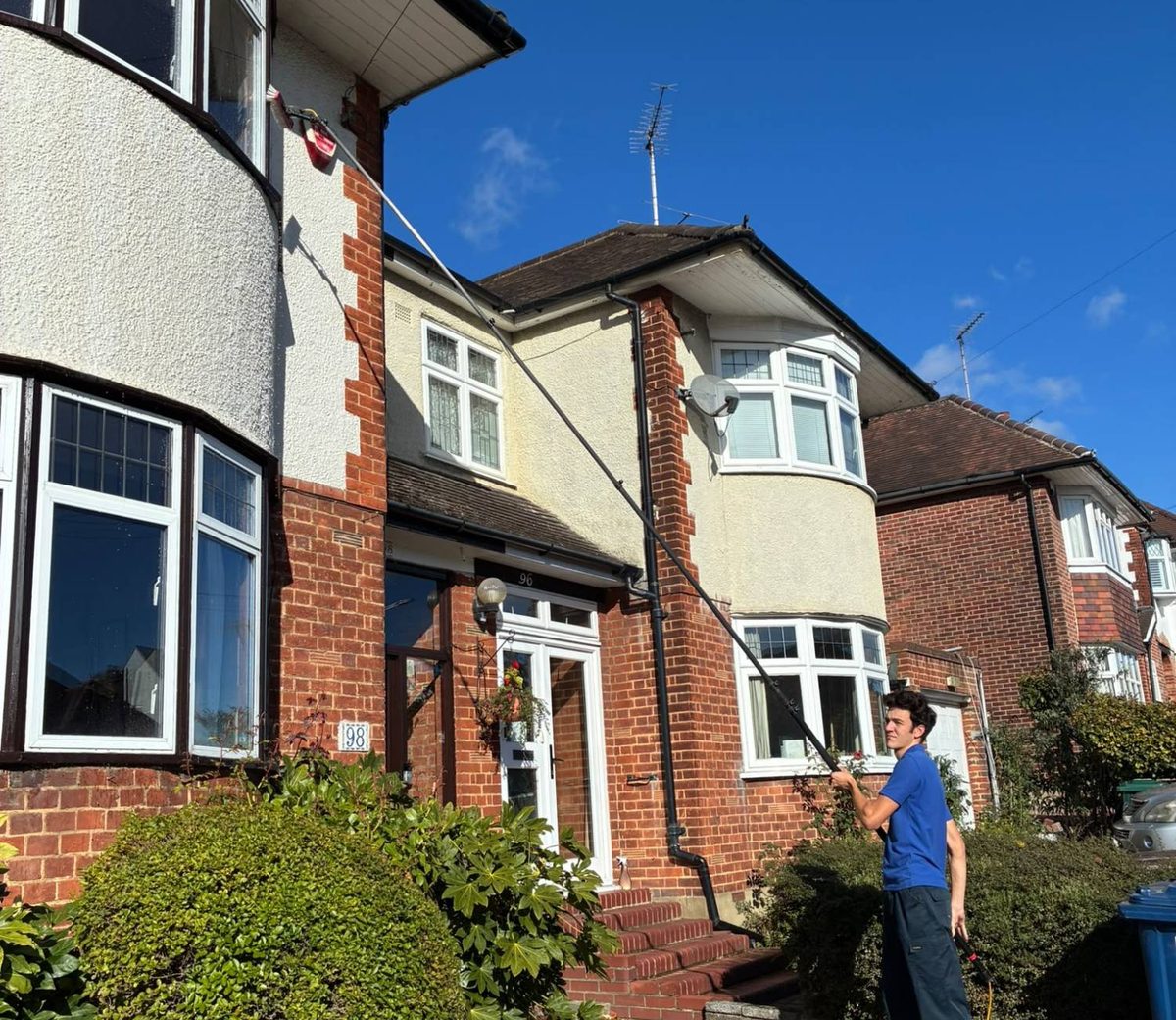 Zac on a driveway reaching the upstairs bay window of a house with a water fed pole