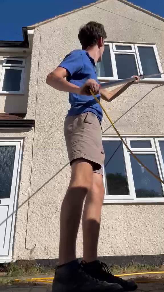 Zac standing on the pavement working a water fed pole to clean the upstairs windows of a house